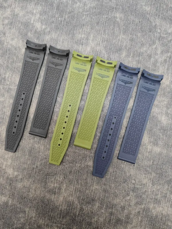Six silicone watch straps in gray, dark gray, olive green, light green, blue, and slate blue laid diagonally on a textured surface, with diamond-patterned grips and Longines branding on the tabs.