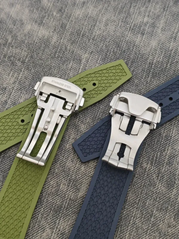 Two silicone watch straps with stainless steel deployant buckles on a textured gray fabric surface, one olive green and one navy blue.