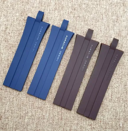 Six flat silicone watch straps in two colors (three blue, three brown) laid out on a beige carpet, branded Porsche Design with looped ends visible.