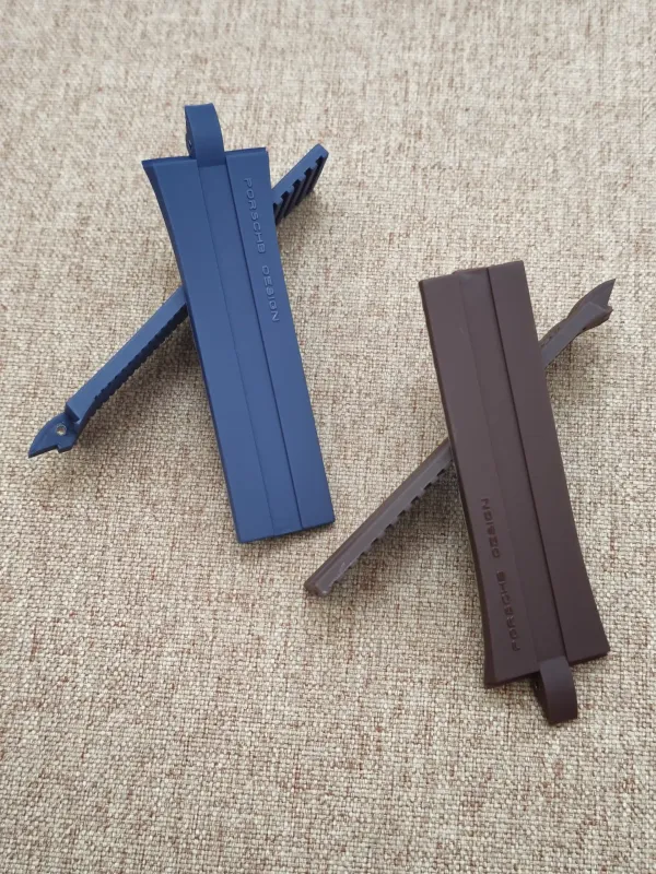 Blue and brown Porsche Design P6360 rubber straps with looped ends, on a beige surface.