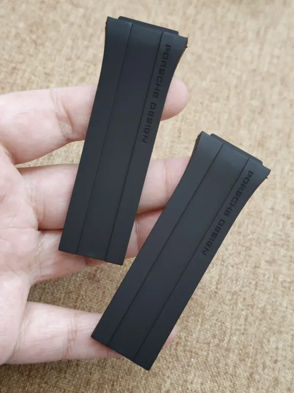 Two black rubber straps for Porsche Design P6780 held in hand, showing the embossed branding.