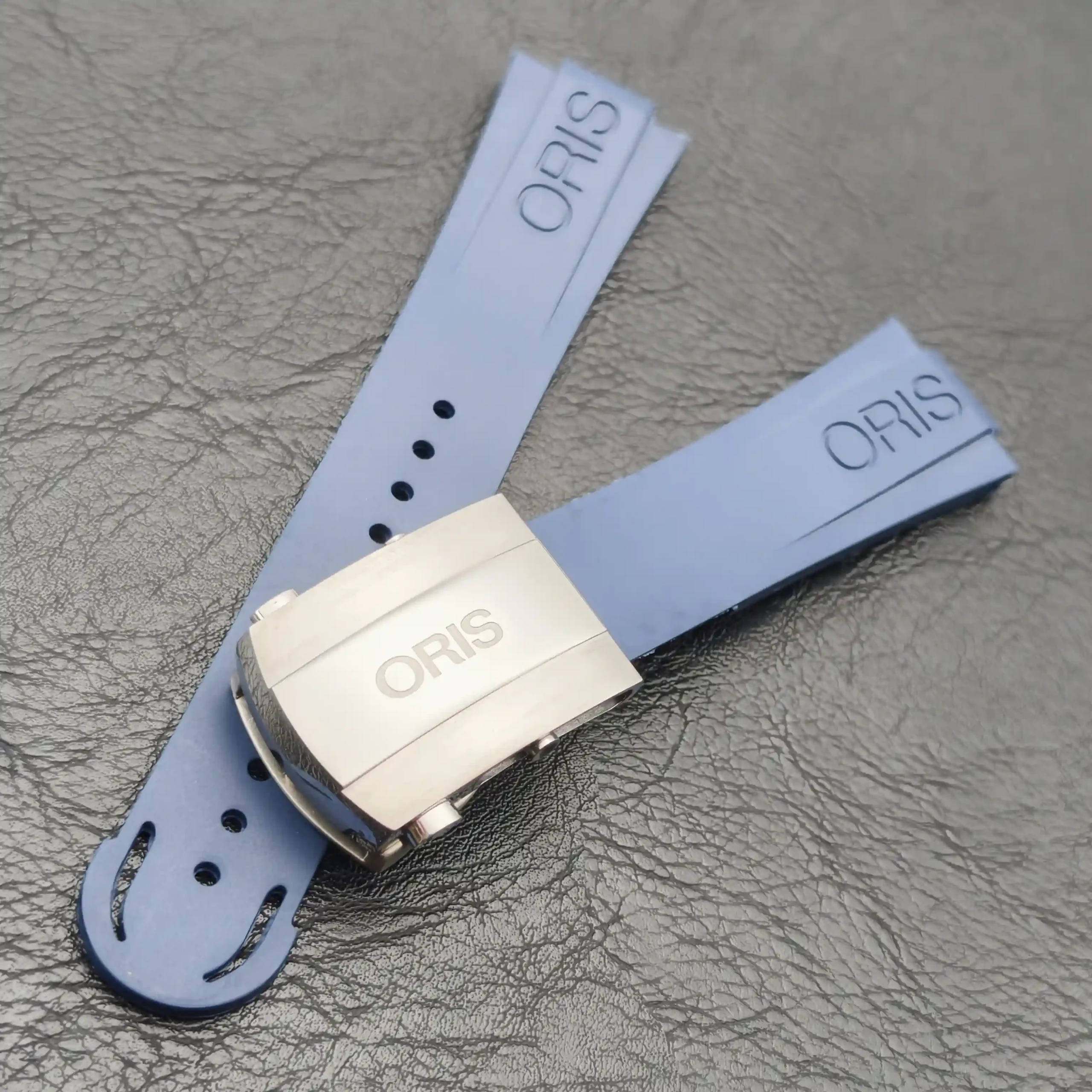 Light blue leather watch strap with a stainless steel buckle and perforated holes, featuring an ORIS tag. (informative product image)