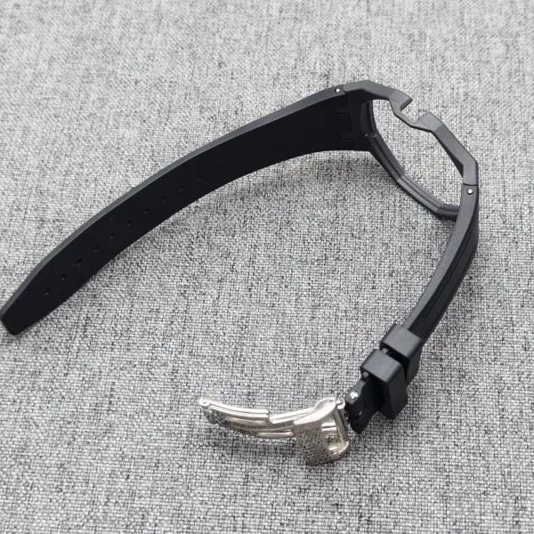 Close-up of a black watch strap with a metal deployment clasp on a gray woven surface.